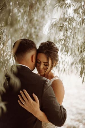 A romantic embrace between a couple surrounded by soft willow branches on their wedding day.