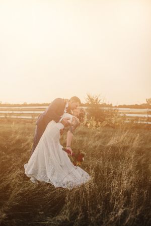 A wedding couple shares an intimate moment at sunset in a field with water in the background.