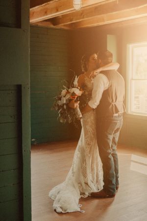 A romantic wedding moment with golden sunlight streaming through a window as a couple embraces in a rustic wooden room.