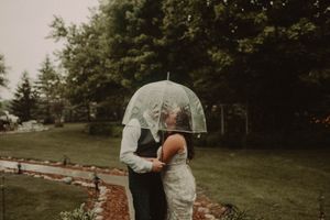 Couple sharing romantic moment under clear umbrella during outdoor wedding.