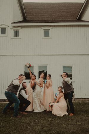 Wedding party poses playfully in front of a white barn during celebration photos.