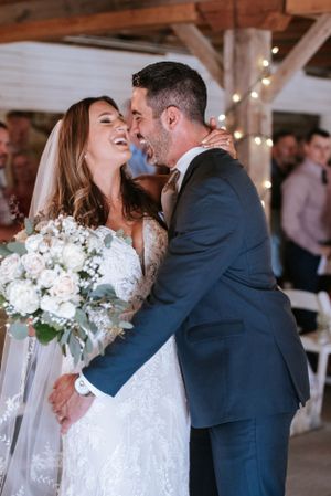 A couple shares a joyful candid moment during their wedding ceremony with the bride holding a white floral bouquet.