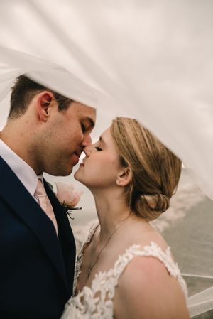 Intimate wedding portrait with flowing white veil against cloudy backdrop.