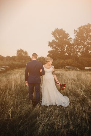 Bride and groom walk through tall grass during golden hour in a rustic field setting.