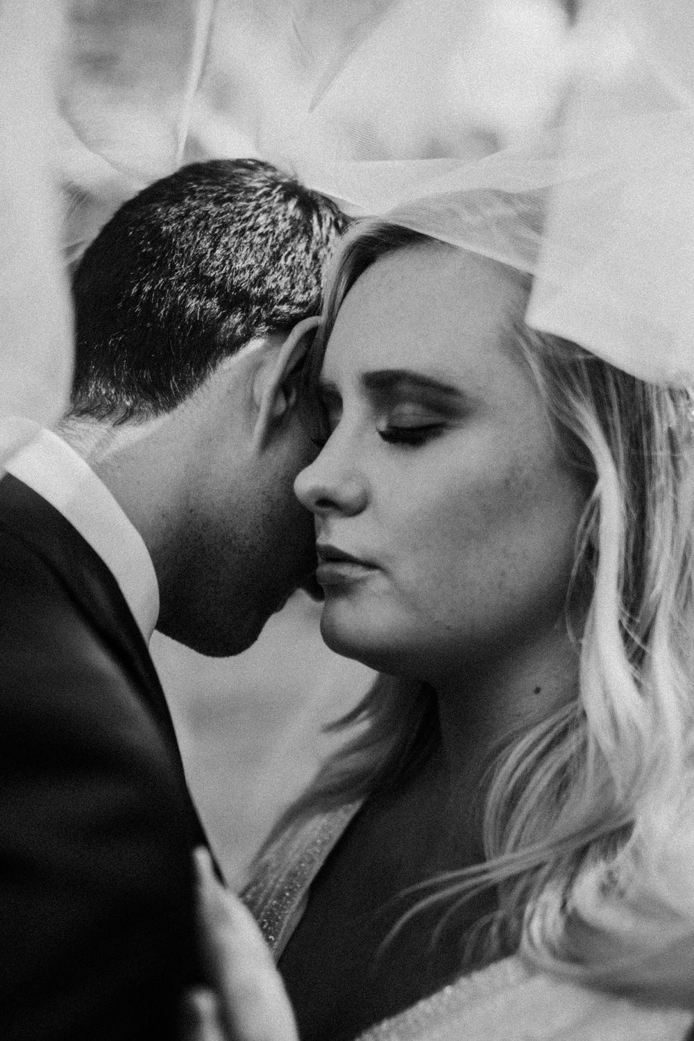 A romantic black and white wedding photo captures an intimate moment between newlyweds sharing a tender embrace.