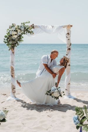 A beach wedding ceremony with birch arch and floral decorations against ocean backdrop.