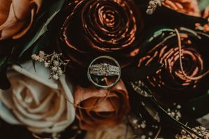 Wedding rings artistically photographed on dark red roses with macro detail.