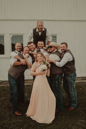 Wedding party poses playfully with bride in blush dress and groomsmen in brown vests.