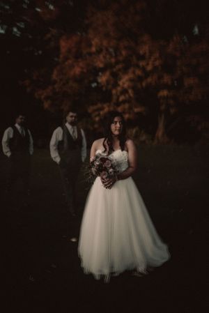 Atmospheric night portrait of a bride in white gown with groomsmen silhouettes in background.