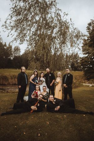 Wedding party poses together under a drooping willow tree in an autumn outdoor setting.
