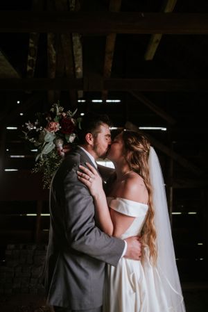 A tender moment between newlyweds in a rustic barn setting with dramatic lighting.