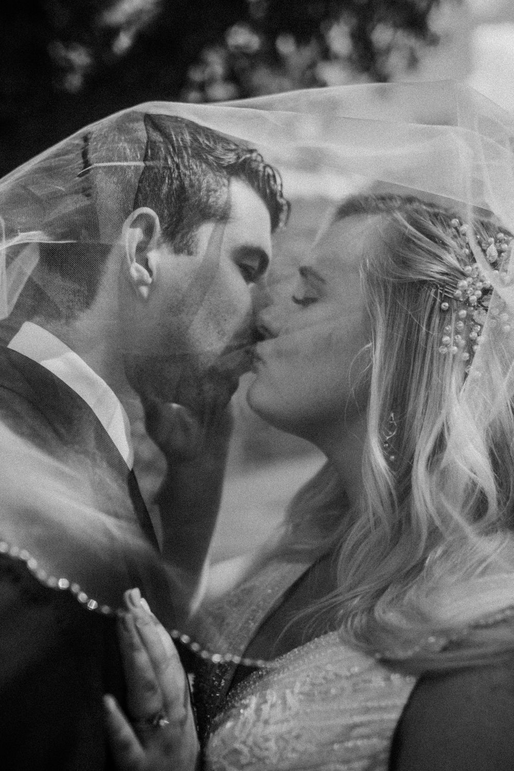 A romantic black and white wedding photo of newlyweds kissing under a delicate veil.