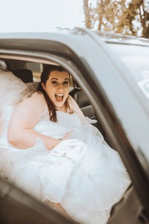 A candid moment of excitement captured in a white wedding dress inside a car.