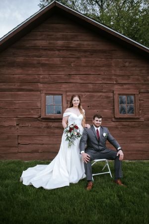 Wedding portrait in front of a rustic red wooden cabin with white trim windows.