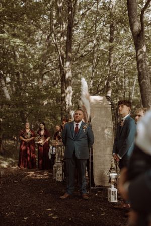 Wedding ceremony setup in wooded area with lanterns and vintage door backdrop.