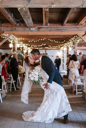 A romantic dip kiss during a wedding reception under twinkling lights in a rustic barn venue.