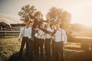 Groomsmen celebrating and lifting someone during sunset at an outdoor wedding venue.