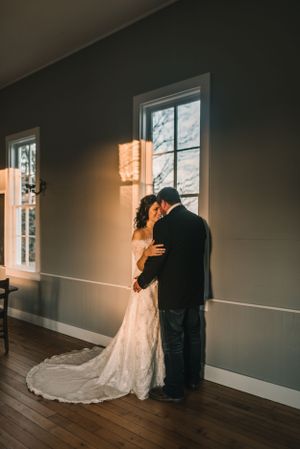 A romantic moment between newlyweds by sunlit windows in an elegant indoor setting.