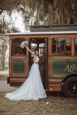 Elegant wedding couple posing in front of vintage trolley car.