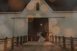 Wedding couple dances on a white chapel's wooden bridge under dreamy bokeh lights.