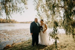 A romantic wedding photo showing a couple under a willow tree by a lake on their special day.