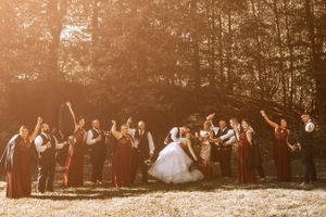 Wedding party celebrating outdoors at sunset with raised hands in joyful group pose.