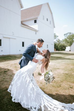 A romantic dip pose in front of a white rustic barn during a wedding photoshoot.