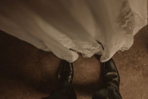Artistic detail shot of wedding dress hem and formal shoes on rustic floor.