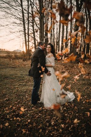 Autumn leaves frame a romantic wedding portrait as sunlight filters through bare trees.