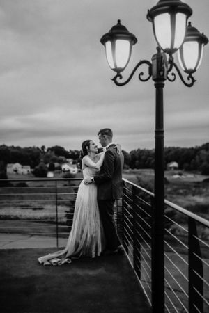 A romantic moment between newlyweds next to a vintage street lamp on a balcony at dusk.