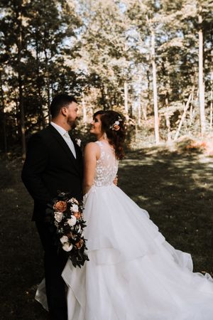 A romantic wedding portrait in a wooded setting with sunlight filtering through autumn trees.