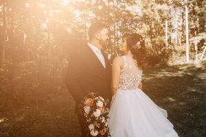 A golden sunset wedding portrait in a forest clearing with floral bouquet.