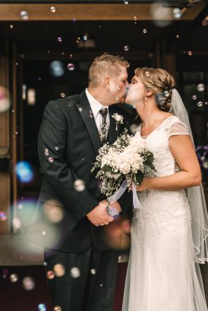 A romantic wedding kiss surrounded by floating bubbles in an indoor venue.