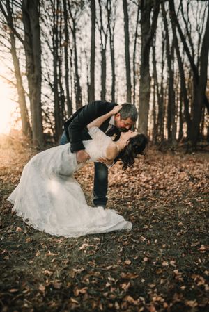 Dramatic dip pose between couple in wooded setting during sunset.