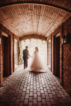 Newlyweds walking through a romantic brick archway with backlit sunlight.