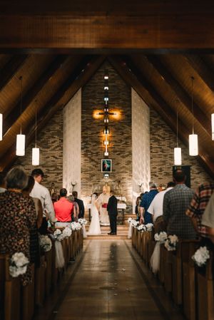 Church wedding ceremony with wooden beams and hanging lights creating a warm ambiance down the aisle.