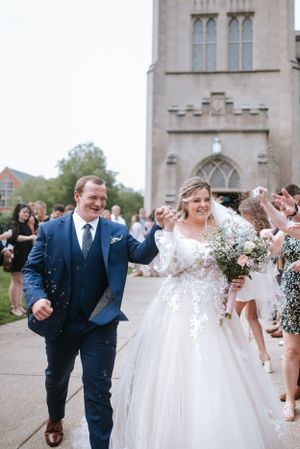 Wedding couple exits church while guests throw confetti along pathway.