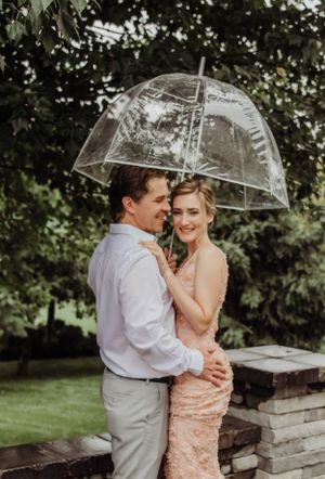 A romantic couple sharing an embrace under a clear umbrella in a garden setting.