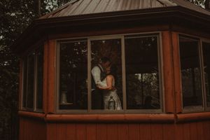 Intimate moment captured through the windows of a wooden gazebo at dusk.