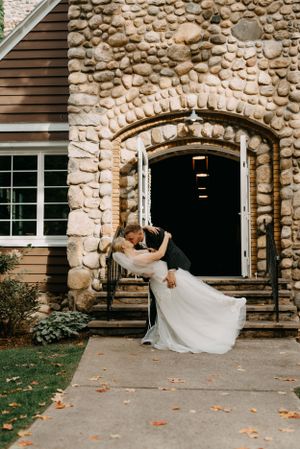 A romantic wedding dip pose in front of a rustic stone archway entrance.