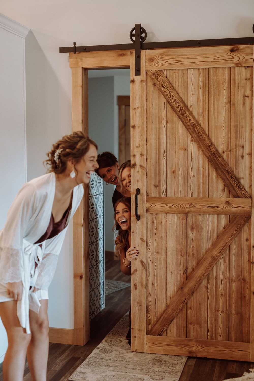 Playful wedding morning moment with people peeking from behind a rustic barn door.