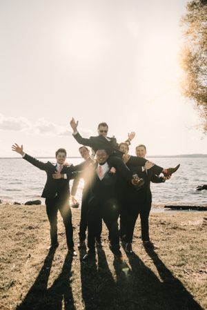 Groomsmen pose playfully on beach at sunset creating dramatic shadows.