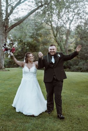Newlyweds celebrate with joyful arms raised on green lawn.