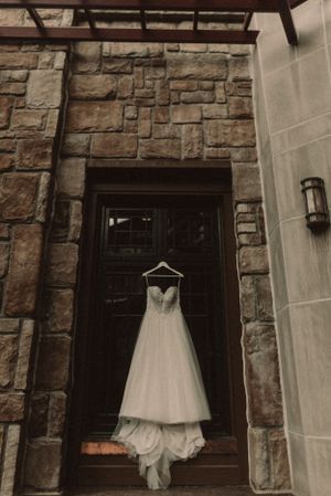 A white wedding dress hanging on a dark wooden door against a stone wall exterior.