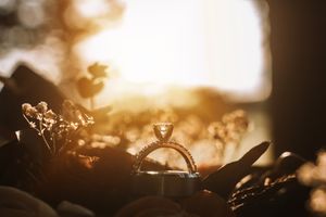 A diamond engagement ring silhouetted against a golden sunset background with delicate bokeh effects.