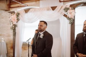 Emotional ceremony moment captured under white draping and floral arrangements in a rustic indoor venue.