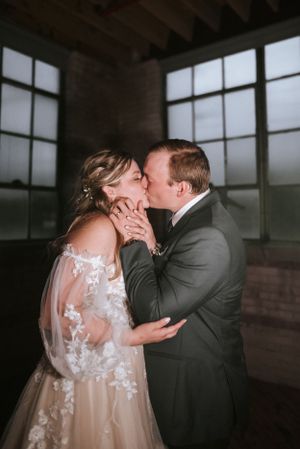 An intimate wedding moment captured between a couple in an industrial-style room with large windows.