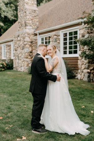 Elegant wedding moment outside stone cottage with white windows and green landscaping.
