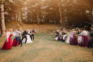Wedding party forms tunnel for couple at outdoor forest celebration.