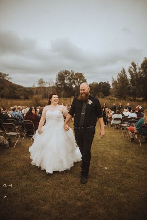 A couple walks down the aisle after their outdoor wedding ceremony with rows of chairs and guests visible.